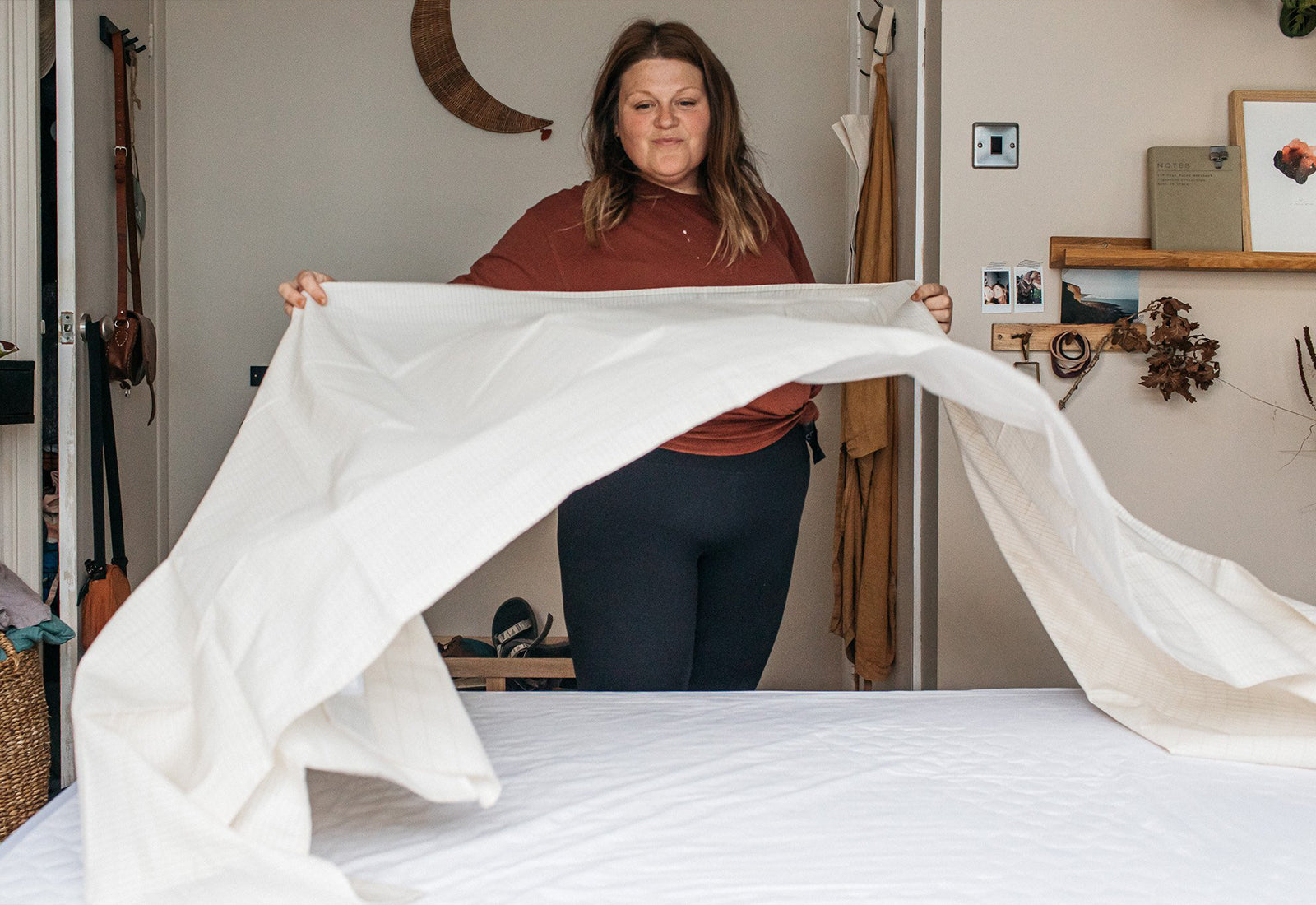 : A woman spreading a grounding sheet over a bed in a cozy, well-decorated bedroom, preparing for a restful sleep
